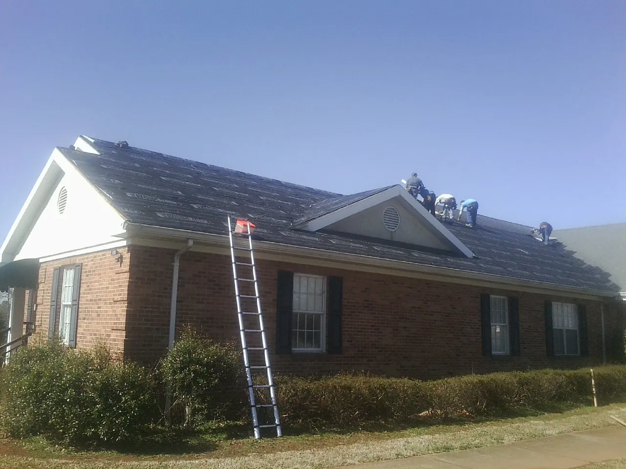 Crew tearing shingles off a brick ranch roof with a ladder set — Emergency Roof Repair work by our crew in Greeley