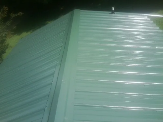 New green metal panels meeting at the ridge of a roof — Flat Roof Repair work by our crew in Greeley