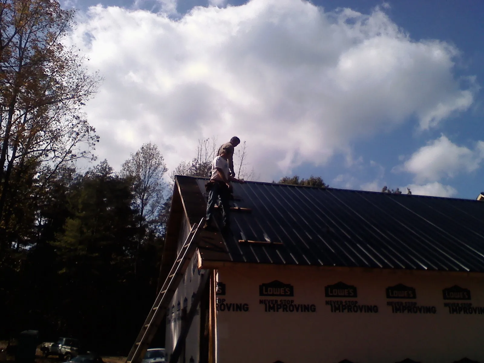 Roofer fastening dark metal panels high against a cloudy sky, from a Roof Inspection job in Greeley